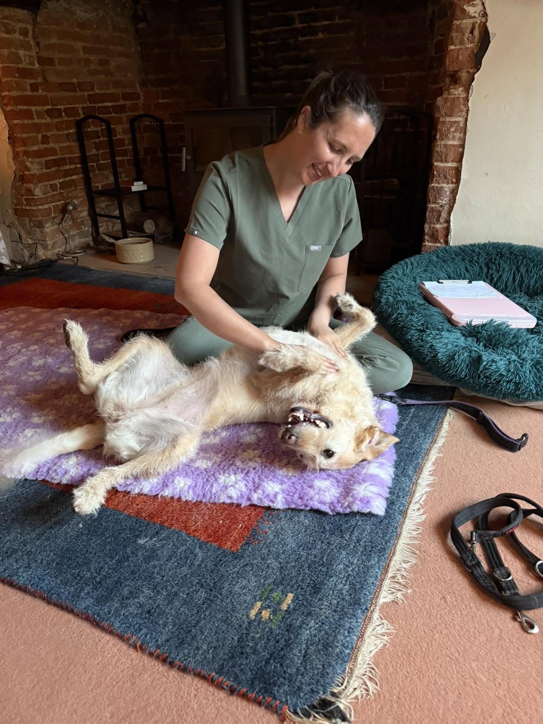 Shanice smiling as a terrier relaxes on a blanket during massage